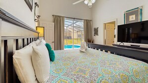 Een slaapkamer met een groot bed, een plafondventilator, een televisie en uitzicht op een zwembad.