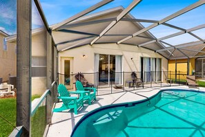 A covered outdoor swimming pool with a glass enclosure, green Adirondack chairs, and a patio area with a table and chairs. - Home in gated community w/private heated pool, air hockey, tennis, clubhouse (Davenport)