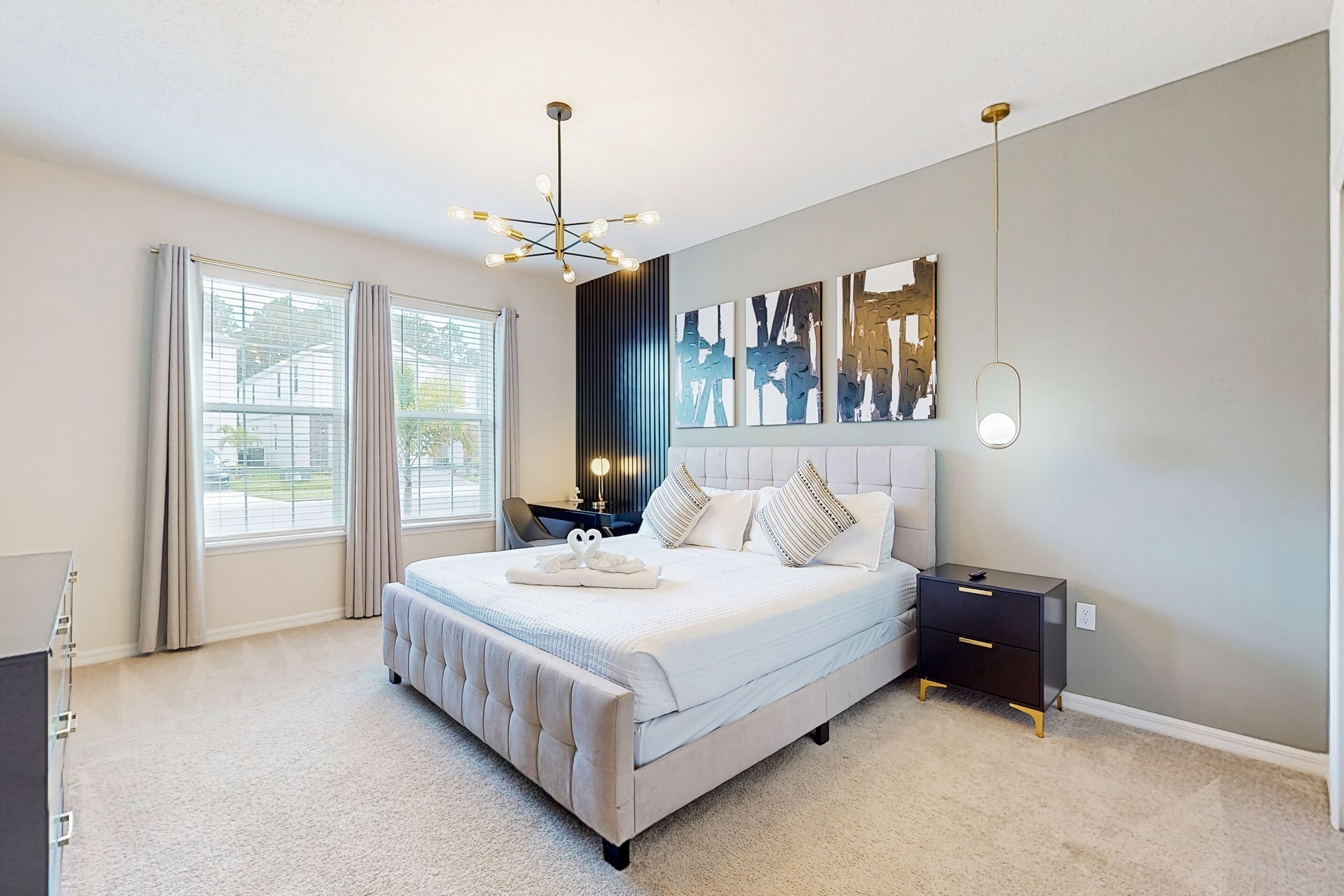 Une chambre moderne avec un grand lit, des tables de chevet, une petite table et un luminaire fixé au plafond.