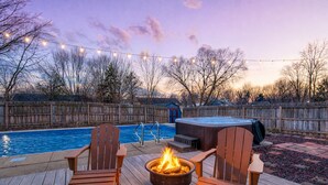 Ein Garten mit Holzterrasse, Whirlpool, Feuerstelle und Schwimmbecken.