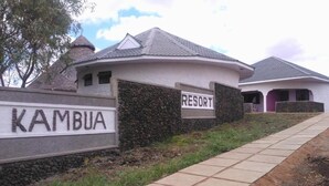 A resort named KAMBUA with a stone wall entrance and a paved pathway leading to the buildings.