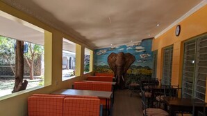 A restaurant with orange booths and tables, a mural of an elephant, and a clock on the wall.