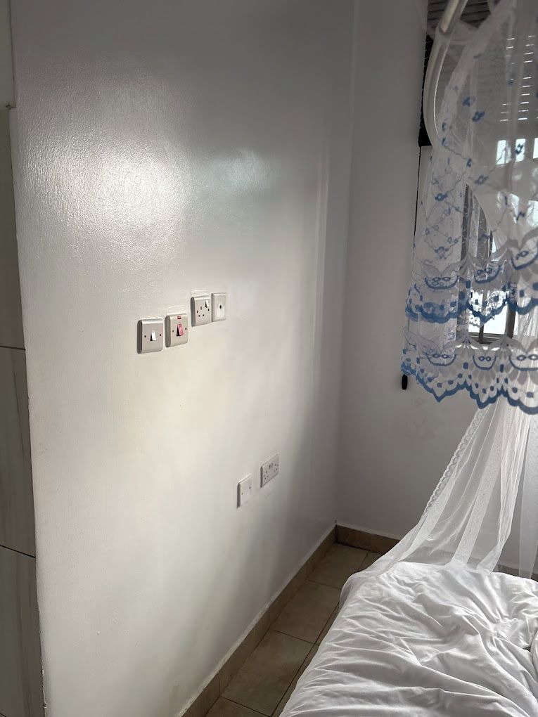 Un dormitorio con cama, pared blanca y toma de corriente.