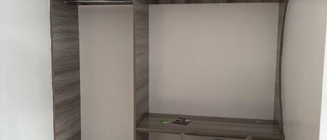 A corner room with a built-in desk and chair, a small shelf, and a wall-mounted light fixture.