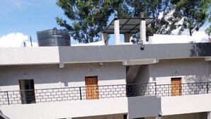 A multi-story residential building with a covered outdoor area, a car parked in front, and a water tank on the roof.