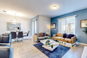 Ein modernes Wohnzimmer mit Sofa, Couchtisch und Sesseln. Es gibt einen Essbereich mit Tisch und Stühlen.