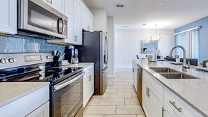 Uma cozinha moderna com eletrodomésticos de aço inoxidável, armários brancos e painel de azulejos.