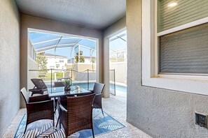 Eine überdachte Terrasse mit Glastisch und Korbstühlen, mit Blick auf einen Swimmingpool und eine Wohngegend.