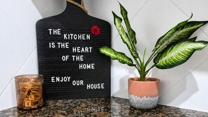 A kitchen backsplash with a black sign stating 'The kitchen is the heart of the home enjoy our house.' - Dog-friendly condo on ground floor with fast WiFi, shared pool, hot tub, & W/D (Davenport)