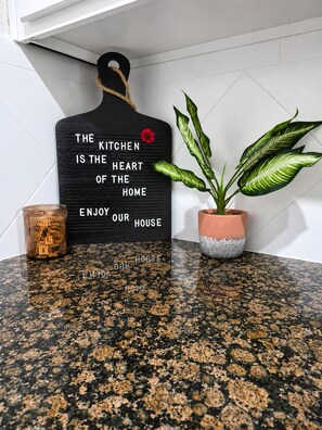 A kitchen backsplash with a black sign stating 'The kitchen is the heart of the home enjoy our house.' - Dog-friendly condo on ground floor with fast WiFi, shared pool, hot tub, & W/D (Davenport)