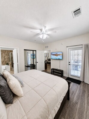 A bedroom with a bed, ceiling fan, TV, and a door leading to a bathroom. - Dog-friendly condo on ground floor with fast WiFi, shared pool, hot tub, & W/D (Davenport)