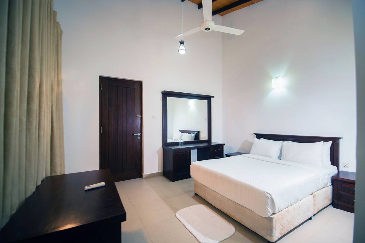 A bedroom with a bed, a desk, a dresser, a mirror, a ceiling fan, and a light fixture.