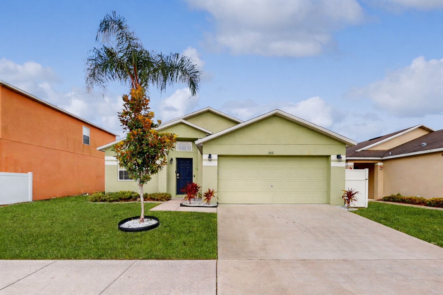A single-story house with a garage, a front lawn, and a small tree.