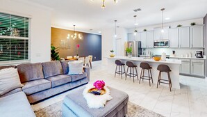Un soggiorno moderno con un divano grigio, un tavolino da caffè con un oggetto decorativo e un'area cucina con pensili bianchi e uno sgabello da bar.