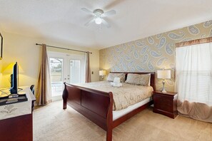 A bedroom with a wooden bed, a desk with a lamp, a ceiling fan, and a window with curtains. - Cozy home with private pool, billiards, central AC and enclosed yard (Davenport)