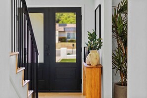 A black door with a view of a building outside, a wooden bench with a potted plant, and a tall potted plant beside the bench. - Spa Retreat: Sauna, Hot Tub & Gym in San Diego (San Diego)