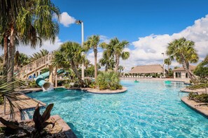 A resort pool area with a water slide, palm trees, and a thatched-roof building. - Artist's Escape at Champions Gate: 5BR/5BA with private pool and resort access (Davenport)