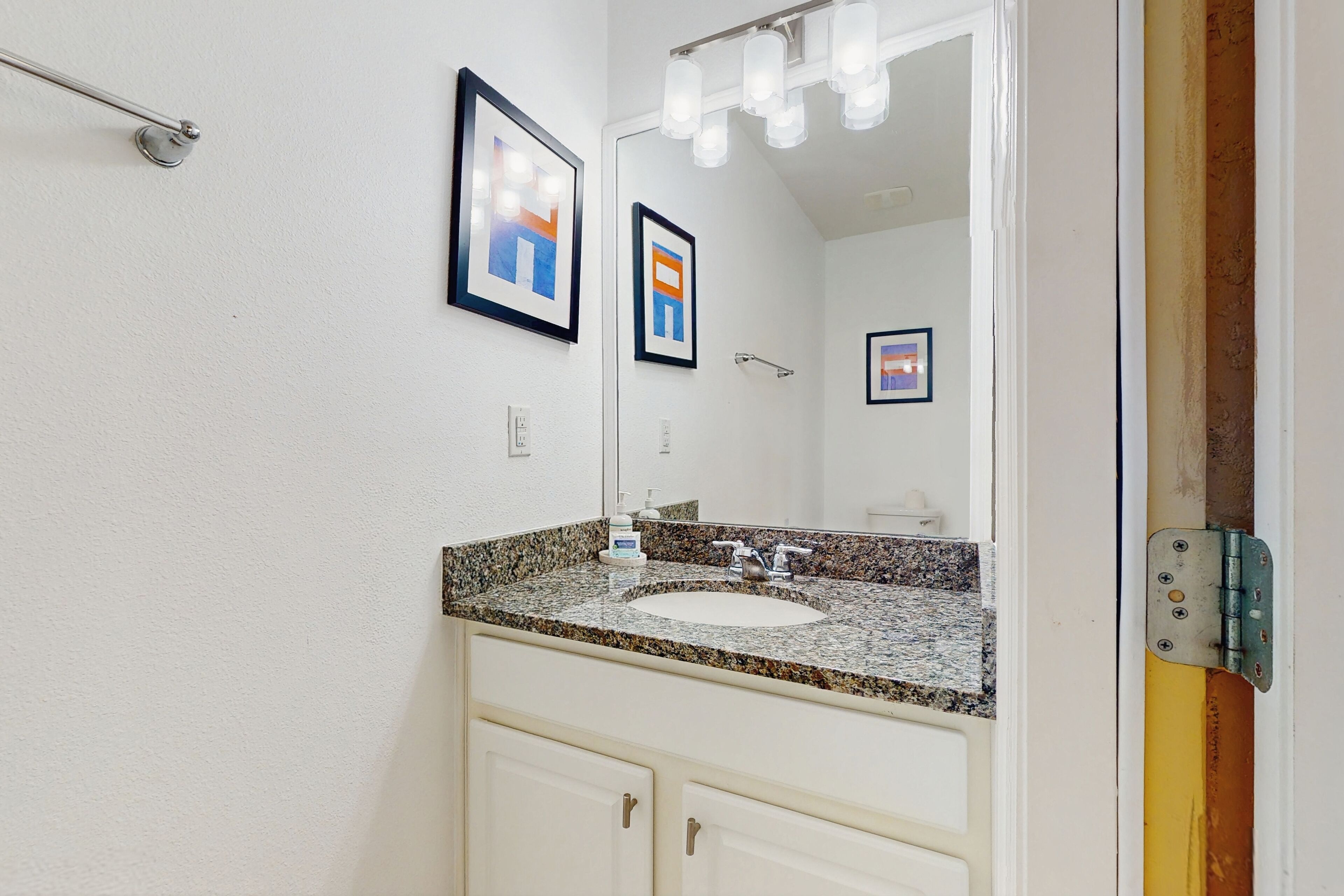 Une salle de bain avec un lavabo surmonté d’un plan de travail en granit, des meubles blancs et un grand miroir.