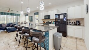A modern kitchen with a central island, bar stools, a refrigerator, microwave, and a coffee maker. - Townhome with private pool in Solterra resort, ADA friendly (Davenport)