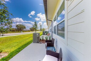 Ein Wohnhaus mit überdachter Veranda, Gartenmöbeln und freiem Blick auf die Straße.