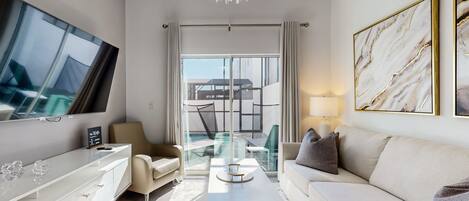 A modern hotel room with a large flat-screen TV, a sofa, a coffee table, and a glass dining table.