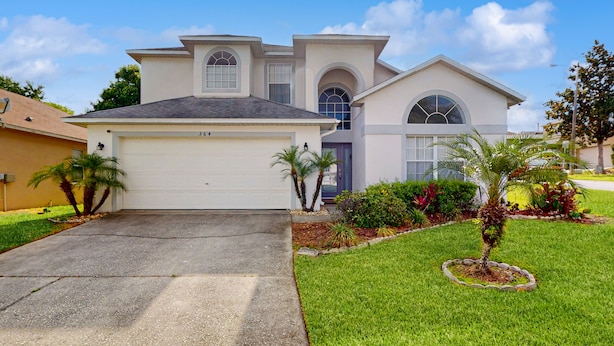 A two-story house with a garage, arched windows, and a well-maintained lawn with palm trees. - Spacious home in cute area with central AC & washer/dryer - snowbirds welcome (Davenport)