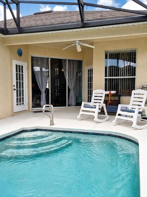 A pool area with a ceiling fan, white lounge chairs, and a glass door leading to a covered patio. - Single-story home with private pool, wifi, central AC, WD and full kitchen (Haines City)