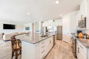 A modern kitchen with white cabinets, granite countertops, stainless steel appliances, and a bar area.