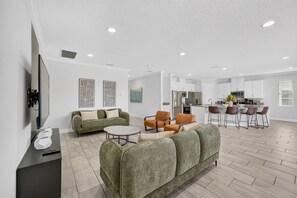 A modern living room with a sofa, coffee table, and chairs, a kitchen with white cabinets and appliances, and a dining area with bar stools. - 13BR/12.5BA Reunion Resort Golf View, Pool, Game Room (Kissimmee)