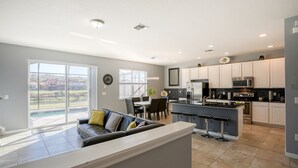 A modern kitchen with white cabinets, a central island, and a dining area with a black leather couch. - Stylish Family Retreat with Pool near Disney World (Kissimmee)