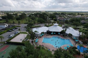 Une grande piscine extérieure entourée de chaises longues et de parasols, avec un court de tennis à proximité.