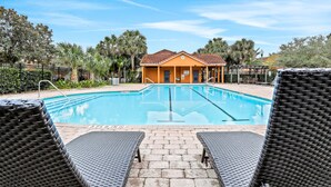 A swimming pool with lounge chairs, a building with a tiled roof, and palm trees in the background. - Dog-friendly townhouse near Disney with outdoor pool, patio, streaming, W/D, AC (Kissimmee)
