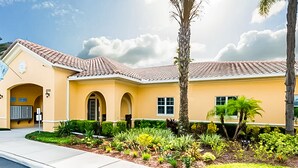 A yellow building with a red-tiled roof, arched doorways, and a landscaped garden with palm trees and shrubs. - Family Home w/Shared Pool,WiFi,AC,Lake Views - Close to Walt Disney World Resort (Kissimmee)