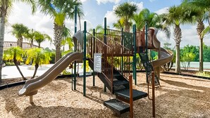 A playground with a slide and climbing structures, surrounded by palm trees and a clear sky. - Family Home w/Shared Pool,WiFi,AC,Lake Views - Close to Walt Disney World Resort (Kissimmee)