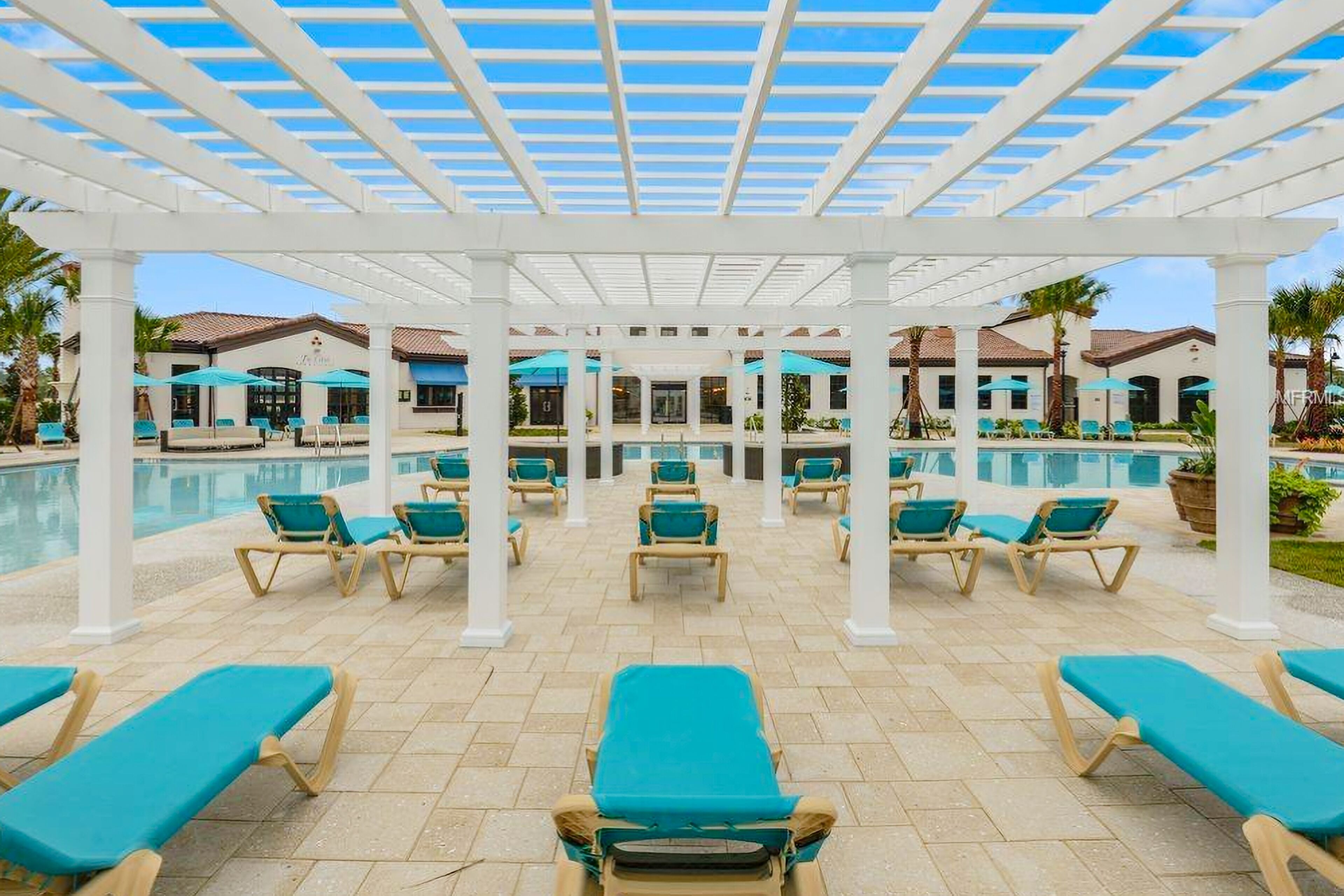 A poolside area with sun loungers and umbrellas, a covered pergola, and a pool.