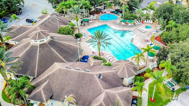 A hotel with a large swimming pool surrounded by palm trees and lounge chairs. There are multiple buildings with similar roof designs. - Resort home with private pool, hot tub, tennis, game room, gym, sports courts (Kissimmee)