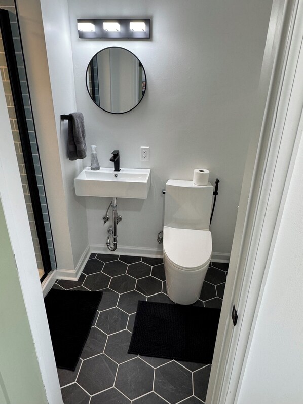A bathroom with a white sink, a toilet, a mirror, and hexagonal patterned tiles. - Cozy riverside 1-bedroom retreat in uptown Maumee! (Maumee)