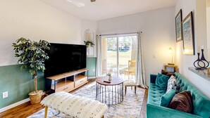 A living room with a flat-screen TV, a round coffee table, a sofa, a ceiling fan, and a large window. - Dog-friendly townhouse with heated pool, lazy river, hot tub, game room, BBQ (Davenport)