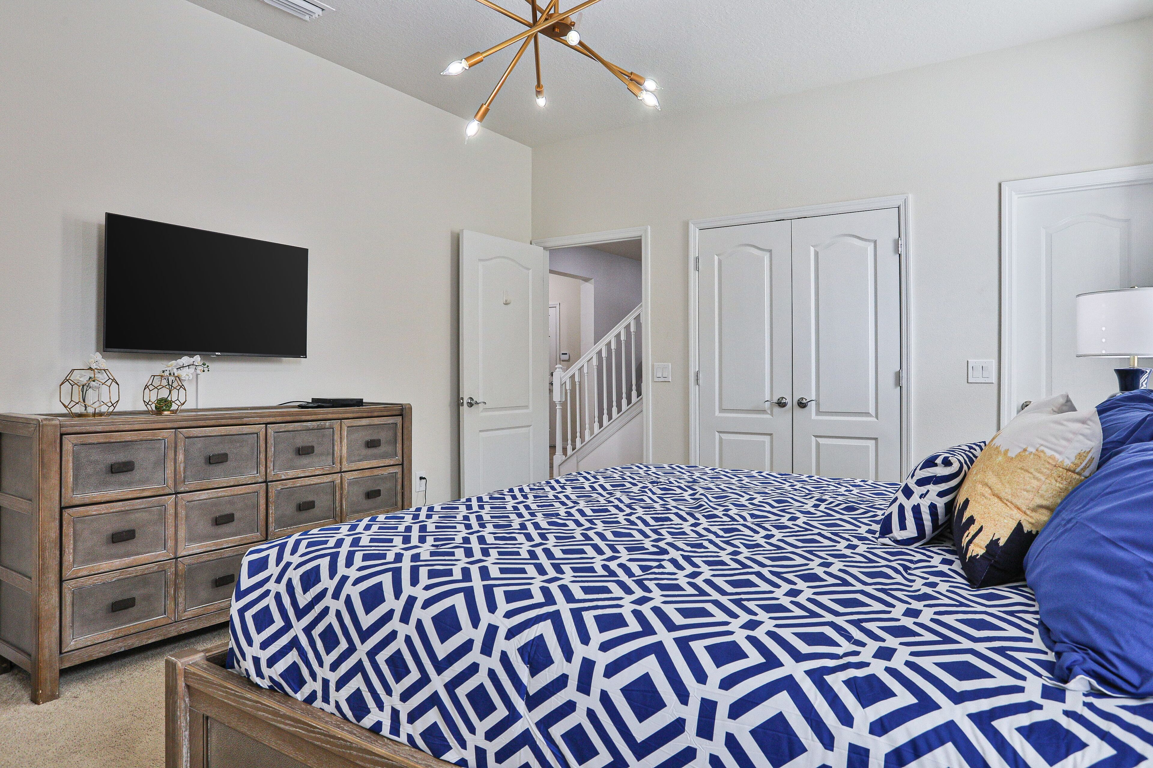 A bedroom with a bed, dresser, TV, and a staircase leading to another room.