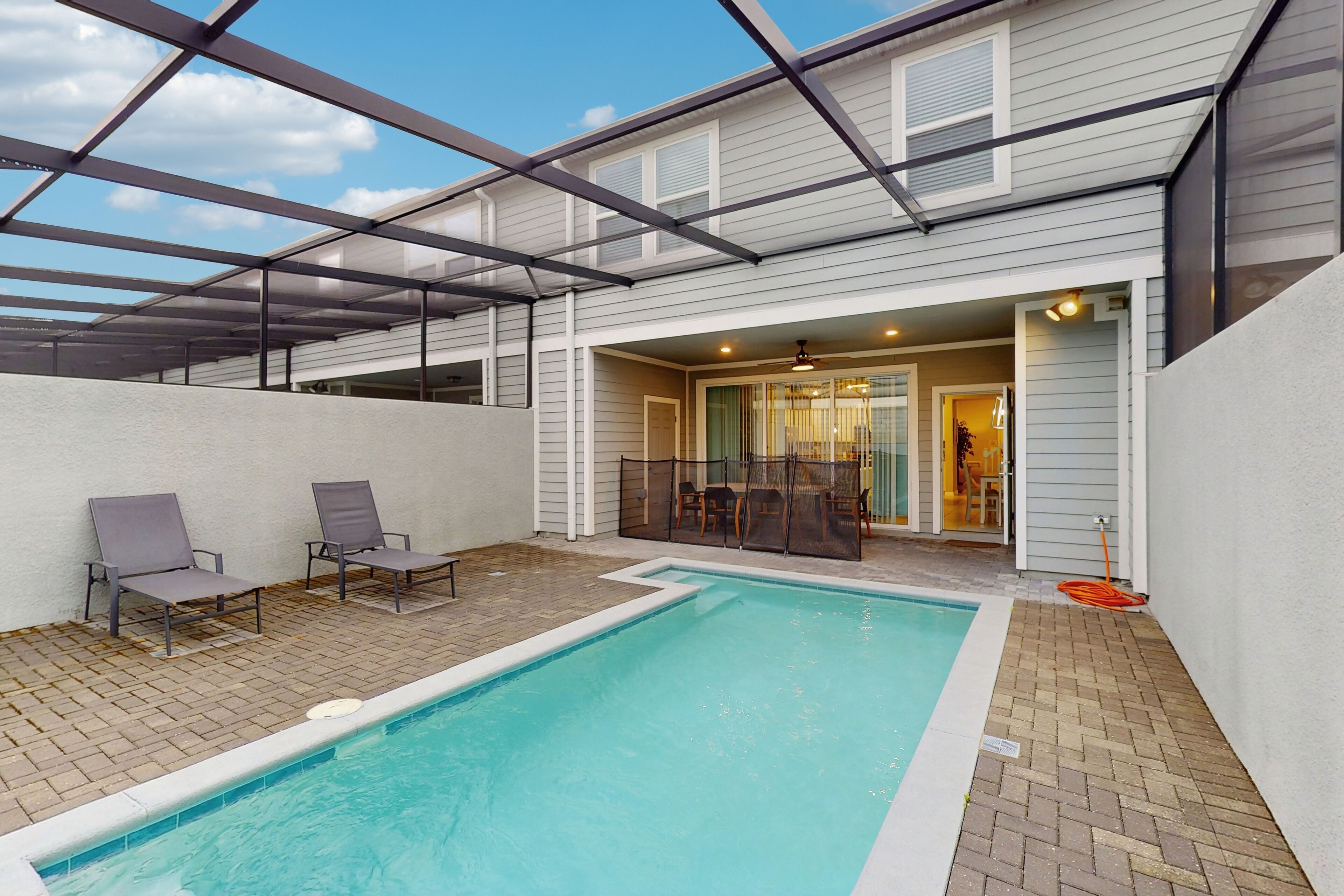 A covered outdoor swimming pool with lounge chairs, a patio area, and a building entrance.