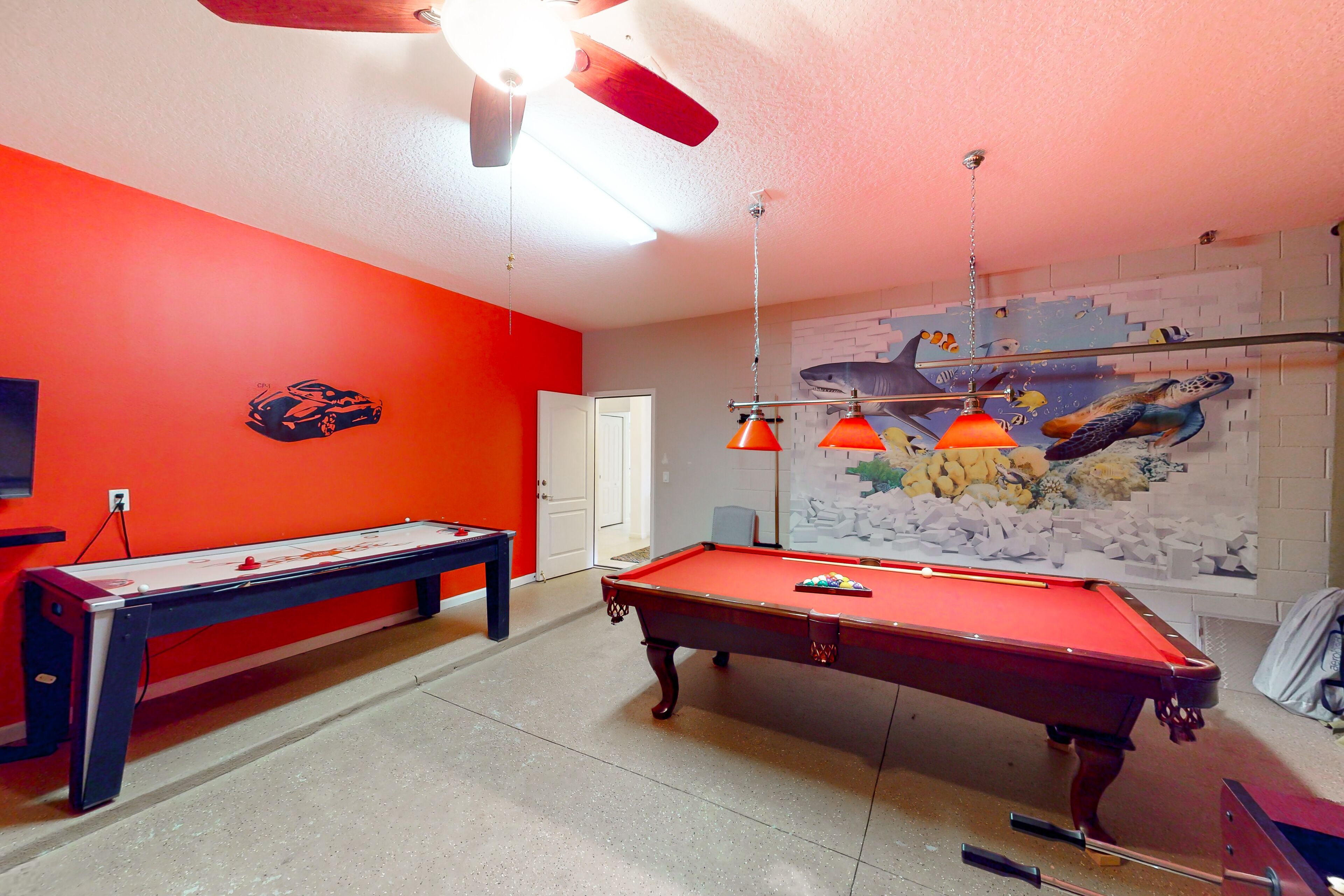 Une table de billard dans une pièce aux murs orange, avec un ventilateur au plafond et une fresque représentant des créatures marines.