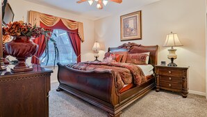 Quarto com cama grande, duas mesas de cabeceira, cômoda, ventilador de teto e janela com cortinas.