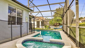 A covered outdoor swimming pool with a hot tub, surrounded by a screened area and a house in the background. - Vibrant modern home with private pool, spa, lanai & expansive game room (Haines City)