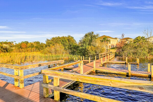 A wooden boardwalk over water with houses in the background. - Tower Lake Hideaway | 4BR Haines City Home, Pool (Haines City)