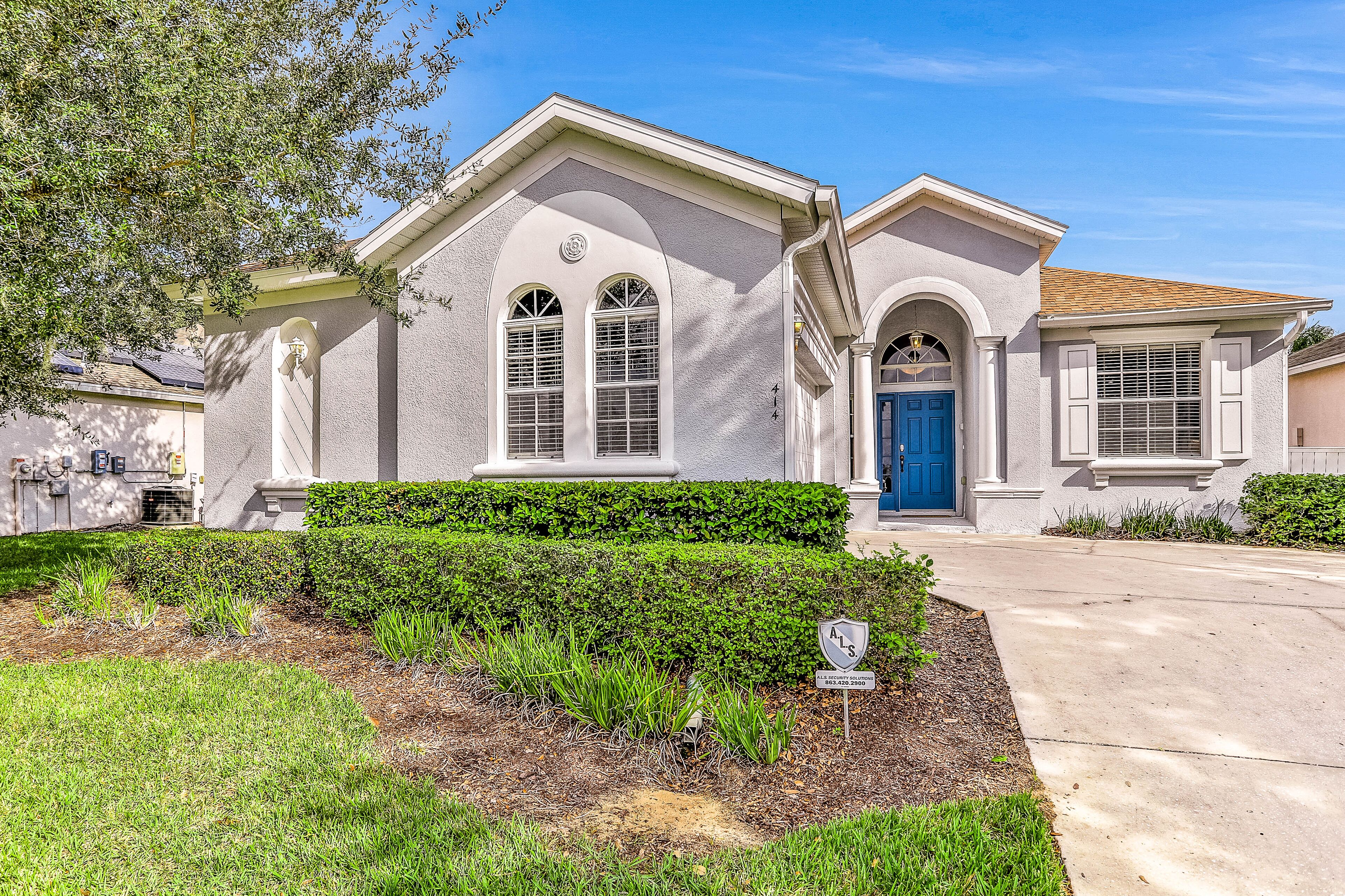 A two-story house with a blue door, white trim, and a well-maintained front yard with hedges and a small garden area.