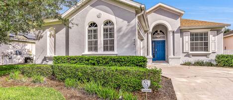 A two-story house with a blue door, white trim, and a well-maintained front yard with hedges and a small garden area.