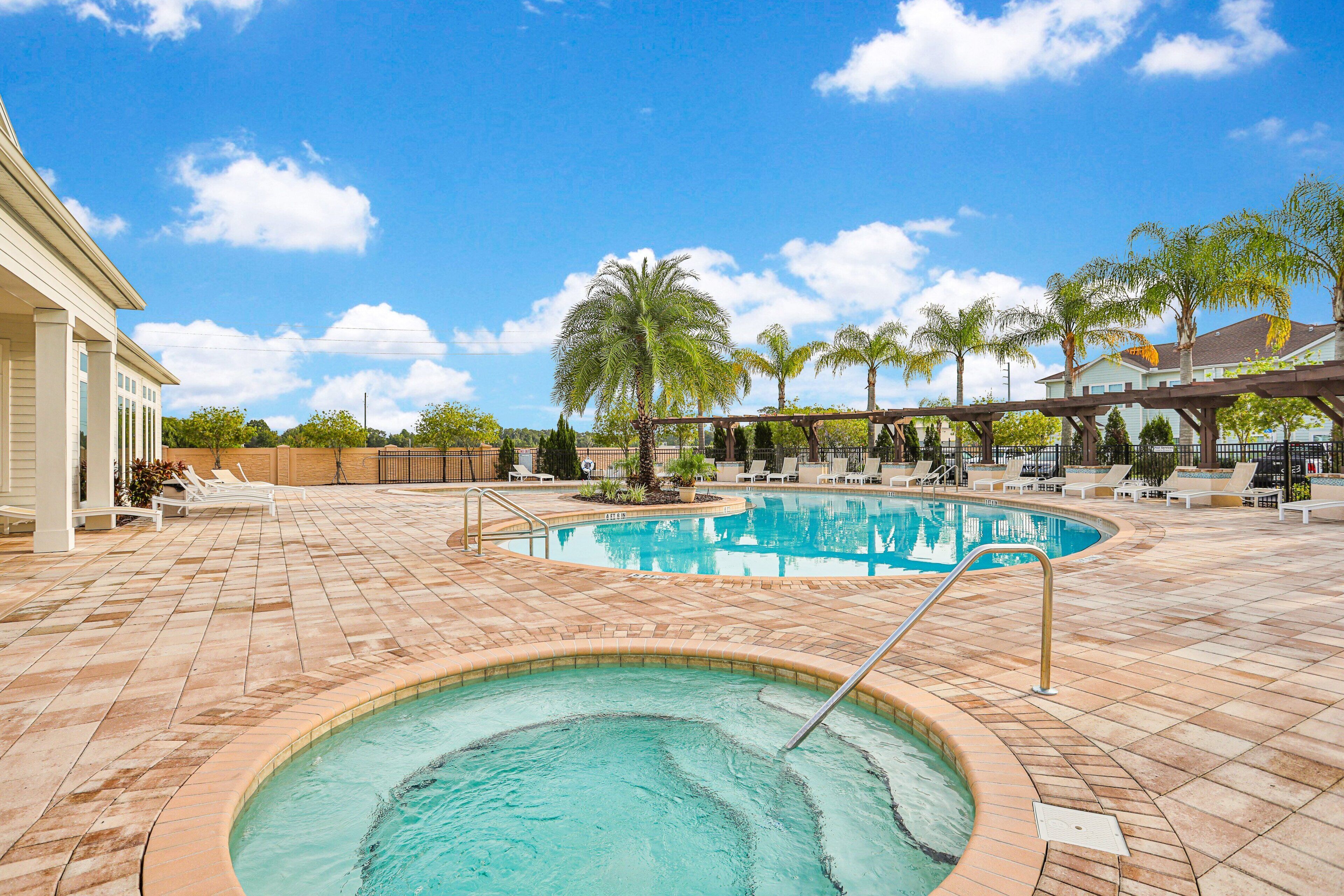 Une piscine avec un jacuzzi, des chaises longues, des palmiers et un ciel bleu azur.