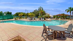 A swimming pool with lounge chairs and a table, surrounded by palm trees and a clear sky. - Comfortable townhome near Disney with athletic courts & pool access, patio, & AC (Davenport)