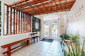 An interior with a wooden bench, two chairs, a wooden pergola with greenery, a tiled floor, and a wall with signage for a bar and grill. - Dog-friendly condo with balcony, pool, W/D, fast WiFi, gym, children's pool, AC (Kissimmee)