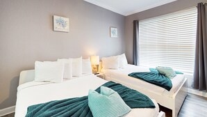 Hotellihuone, jossa on kaksi sänkyä, suuri ikkuna, jossa on sälekaihtimet, sekä kaksi seinälle kiinnitettyä taideteosta.